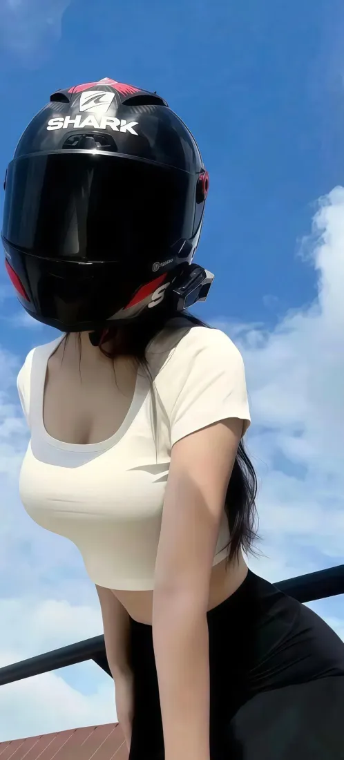 戴黑色机车头盔的女性，穿米白短上衣黑长裤，蓝天户外背景。