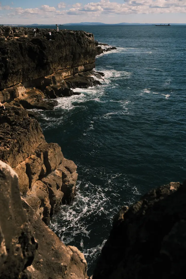 滨海悬崖礁石俯瞰蔚蓝深海，白浪拍岸，远海可见货轮与云天