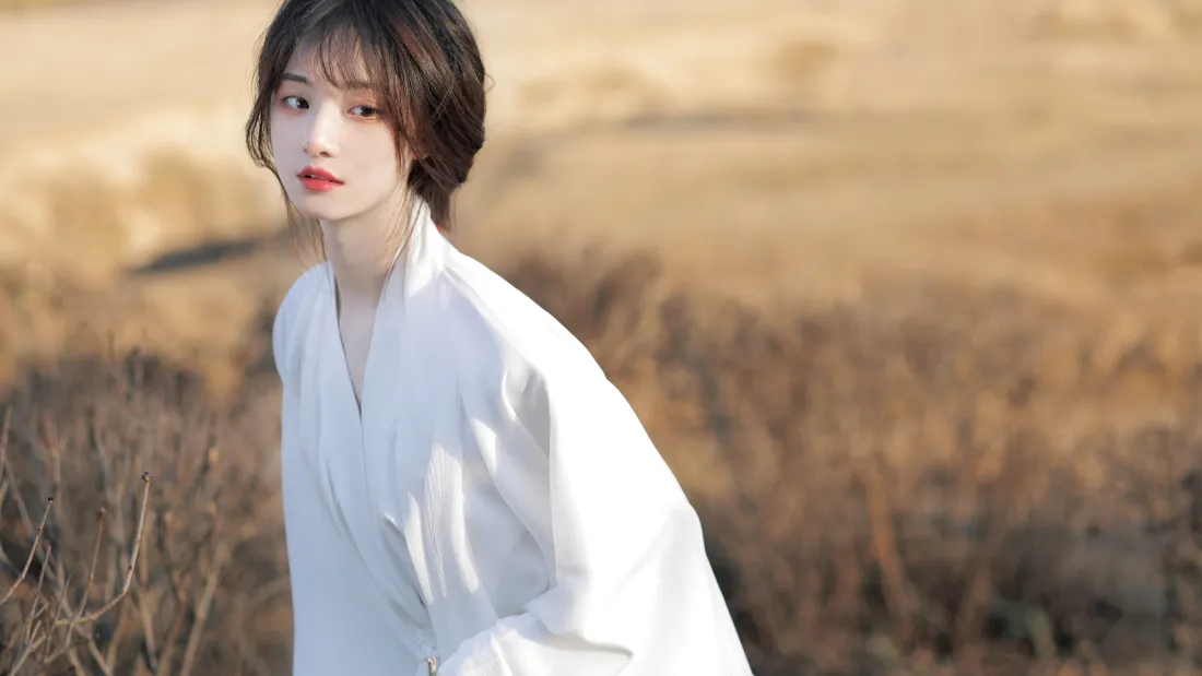 秋日枯黄郊野中，身着白衣的短发少女侧身回望，暖光柔和。