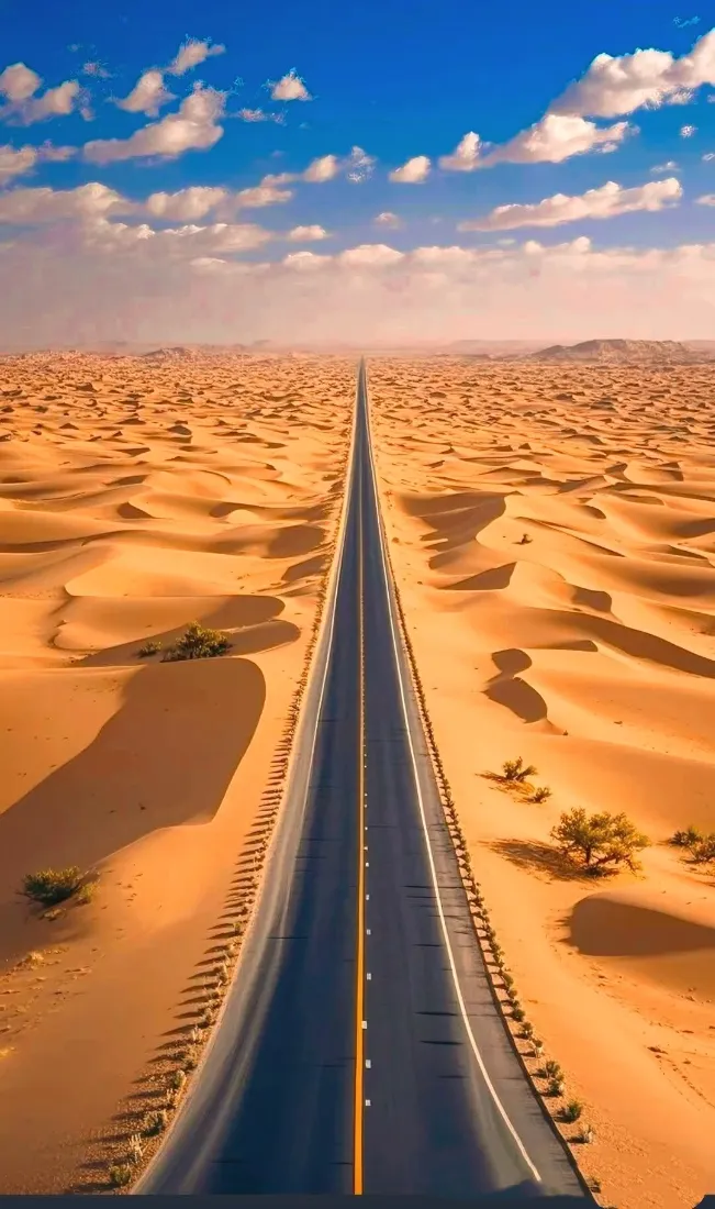 笔直公路纵穿金黄沙漠，上方是点缀白云的湛蓝晴空