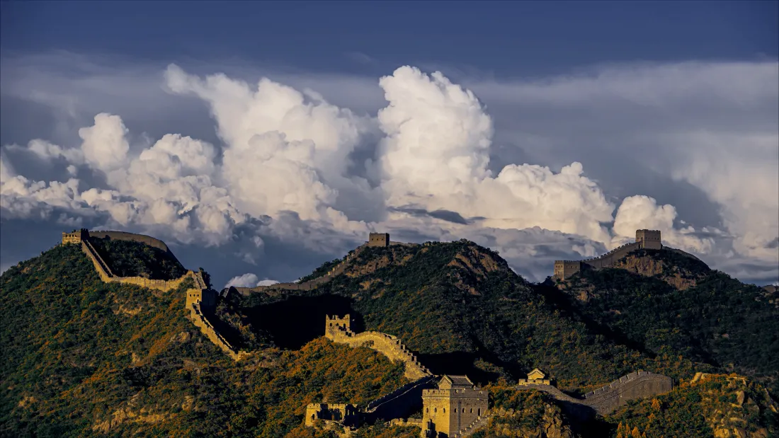蜿蜒长城盘踞在覆满绿植的山峦之上，上方是蓝天与大朵白云