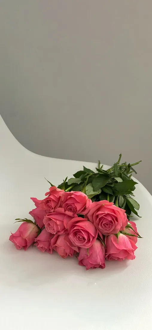 灰色墙面前的白色台面上，摆放着一束带绿叶的粉玫瑰花束。