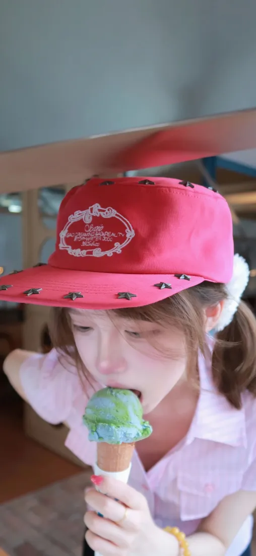 戴粉色棒球帽的双马尾少女，手持双色冰淇淋甜筒凑近嘴边