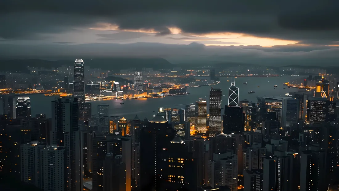 暮色阴云下的香港维多利亚港，两岸摩天大楼灯火璀璨，海湾静谧开阔。