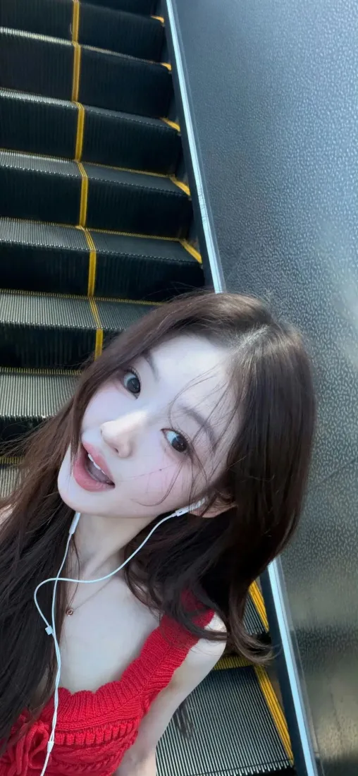 穿红色吊带的长发少女在自动扶梯上戴白色有线耳机自拍