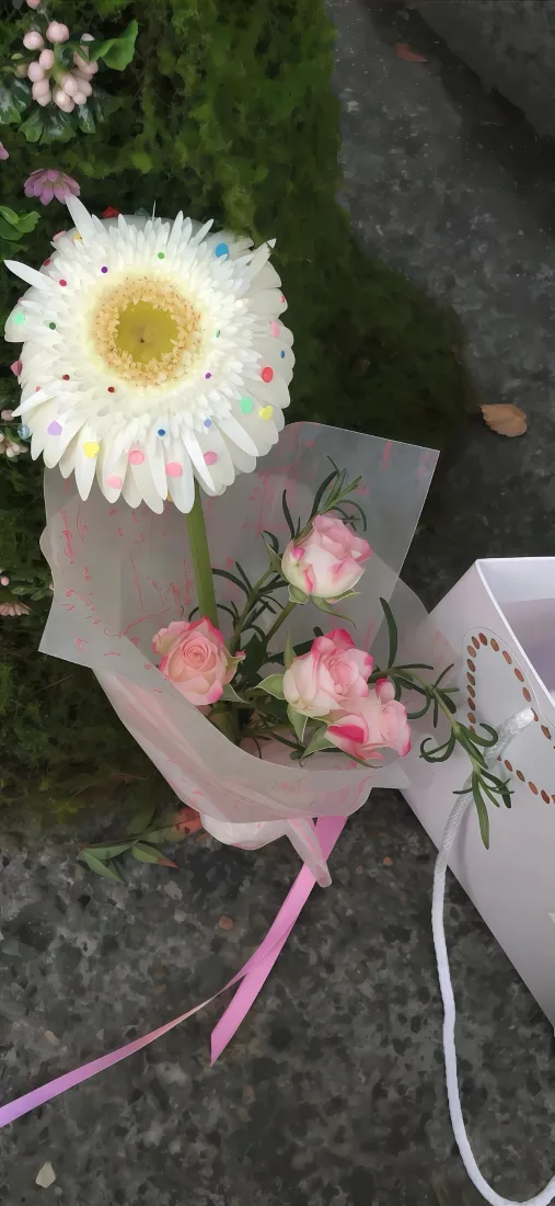 户外地面上摆放着装饰彩点的白色扶郎花束，旁侧有白色礼品袋