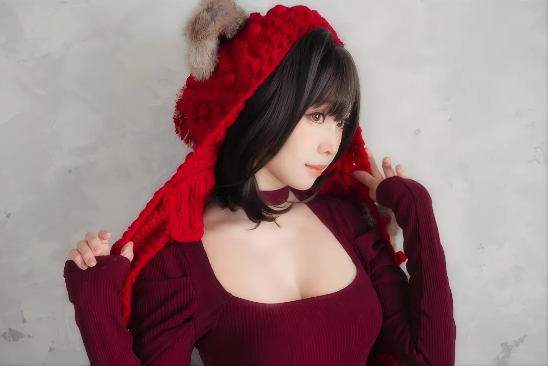 短发女性戴带毛球的红色针织帽，穿酒红色方领上衣，靠在白墙前侧身看向画面右侧