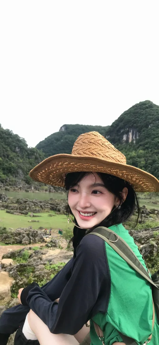 戴草帽的田曦薇在山野间回头甜笑，背景是青山草地。