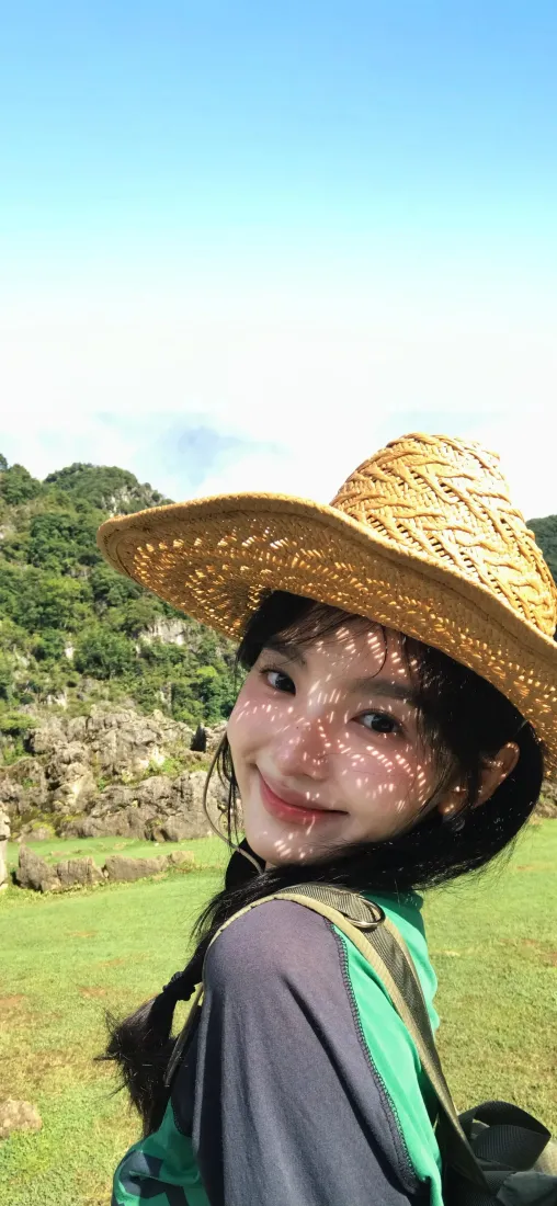 戴草帽的田曦薇在青山草地间回眸微笑，阳光洒落，氛围清新治愈。