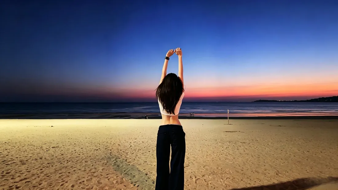 3k海边少女壁纸|日落沙滩背景图片 - 治愈氛围感背影「哲风壁纸」 日落时分的沙滩上,长发少女背对镜头伸懒腰,面朝渐变晚霞与大海。