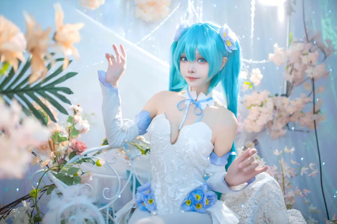 8k初音未来cos壁纸|花艺布景背景图片 - 蓝发美女「哲风壁纸」 蓝发双马尾初音未来coser身着白裙,置身粉蓝花艺布景中抬手微笑