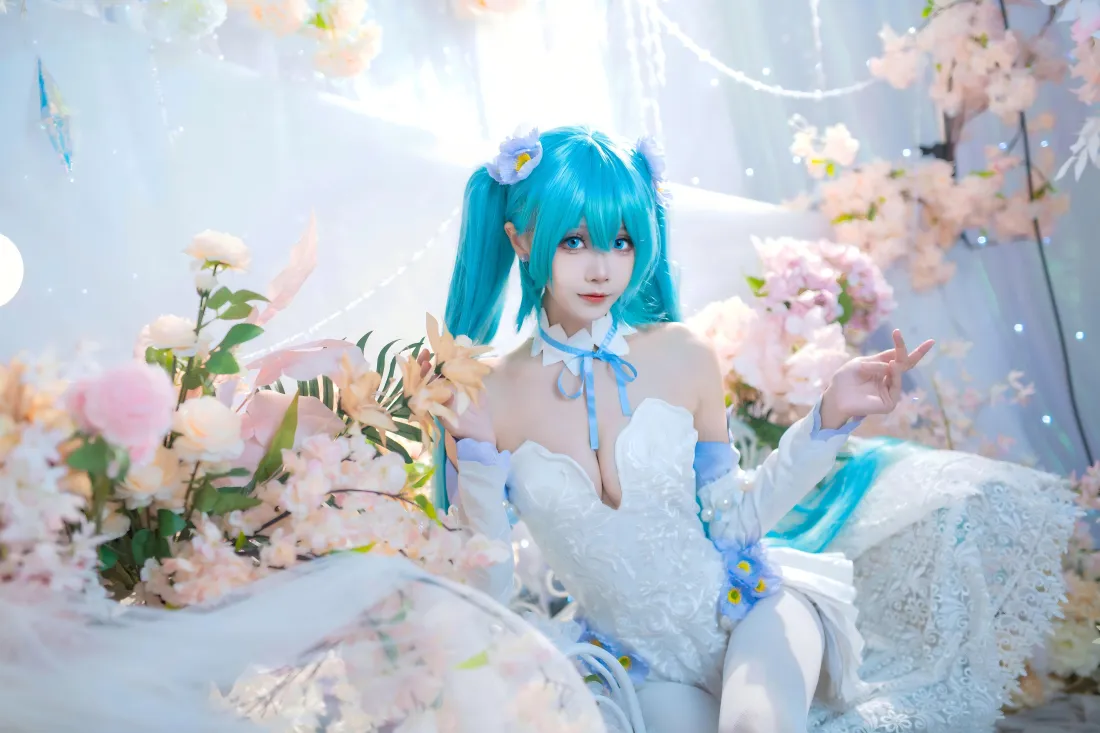蓝发双马尾初音未来coser身着白色露肩礼服，置身粉色花簇中