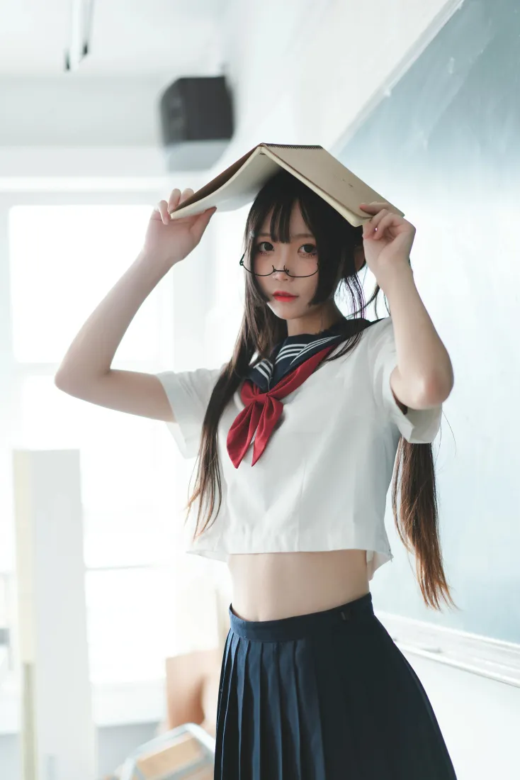 戴眼镜的水手服少女在明亮室内，将书本举在头顶，俏皮可爱。