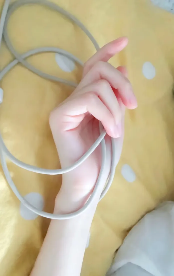 手部特写，手缠绕灰色数据线，背景为黄色波点床单