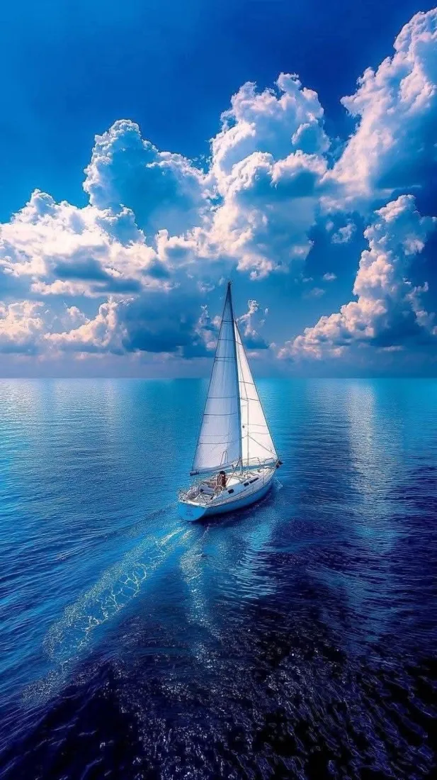澄澈蓝海上，一艘白帆帆船静静航行，天空点缀蓬松白云，海天一色开阔辽远。