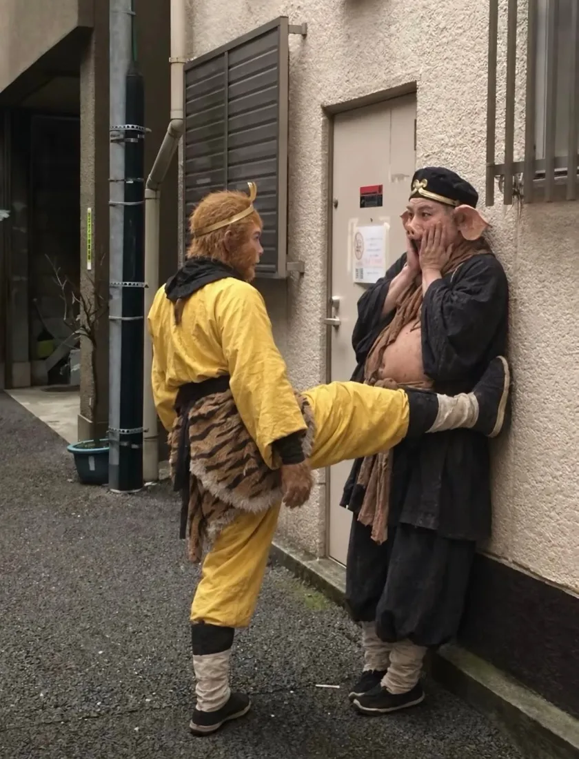 小巷中悟空coser抬腿抵住靠墙的八戒coser，八戒双手捂脸露出惊讶神态。