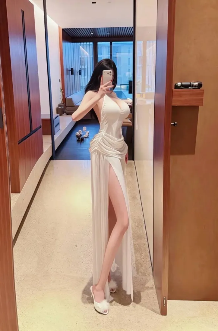 黑长直女子穿白色挂脖高开叉长裙，在室内走廊对镜自拍。