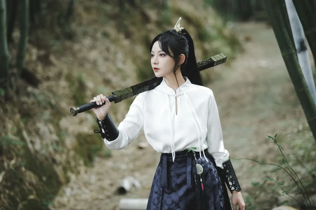 4k武侠风女生壁纸|竹林户外背景图片 - 持剑江湖「哲风壁纸」 竹林间高马尾侠女肩扛佩剑,着白上衣藏青裙,望向画面左侧。