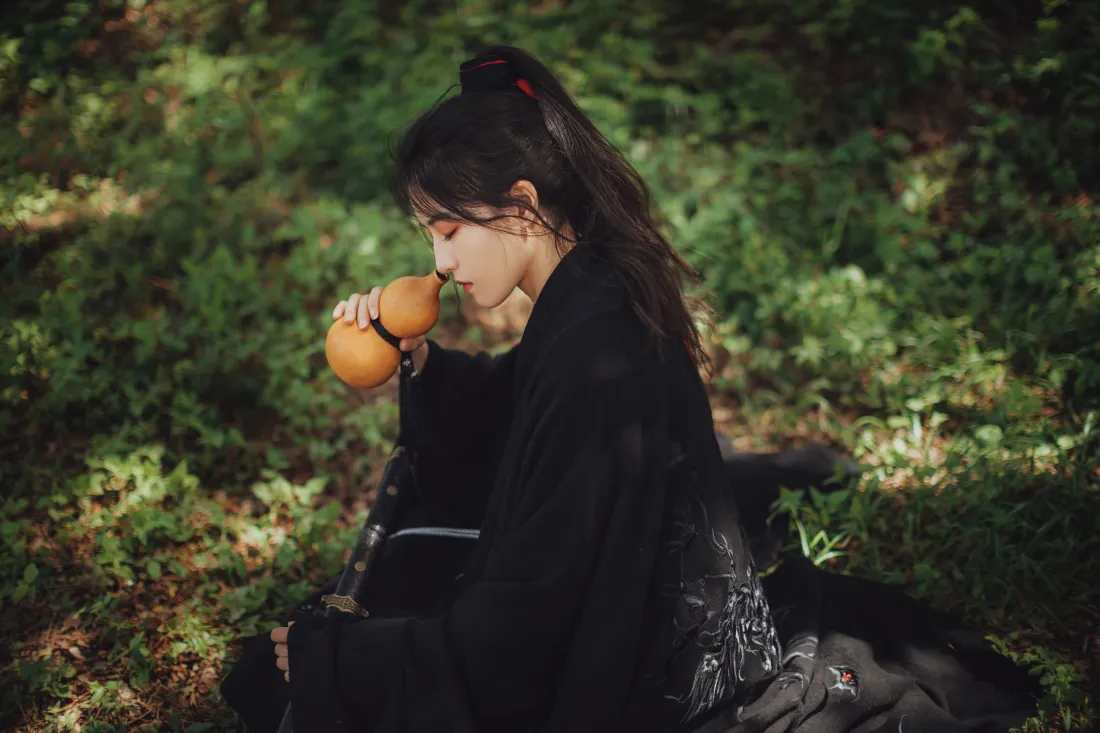 林间黑衣古风女子坐于绿植间，持葫芦饮酒，氛围悠然江湖。