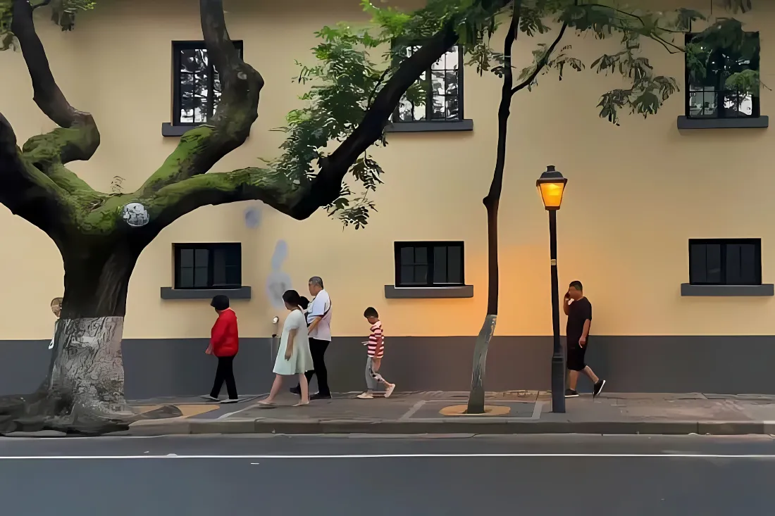 南京颐和路暖光街景，黄墙民国建筑前人行道上有行人漫步。
