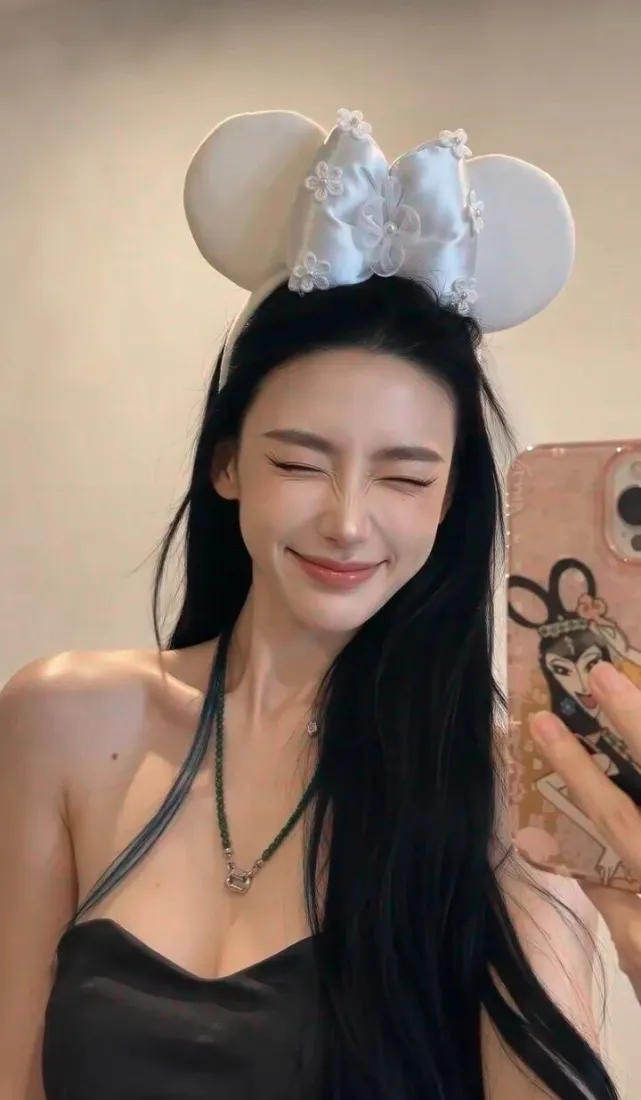 戴米妮耳发箍的黑长直女生对镜自拍，闭眼甜笑，穿黑色挂脖吊带