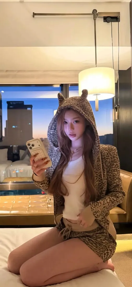 长发美女穿豹纹恶魔角连帽外套，在酒店卧室床上跪姿对镜自拍。