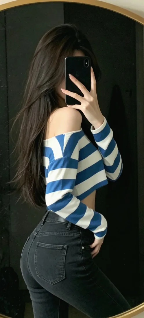 长发美女对镜自拍，穿蓝白条纹露肩上衣与深色紧身牛仔裤，手持手机遮挡面部。