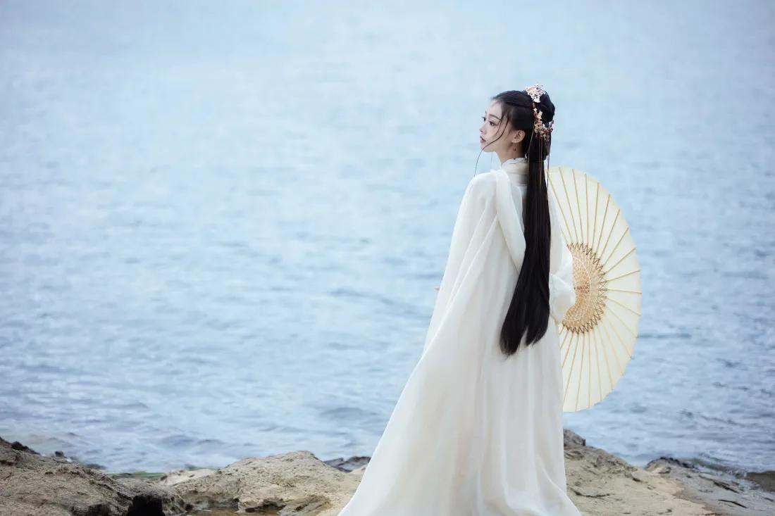 4k古风白衣女子壁纸|水边纸伞背景图片 - 河畔回眸「哲风壁纸」 白衣汉服女子立于水边礁石,手持油纸伞回眸,背景是淡蓝水面。