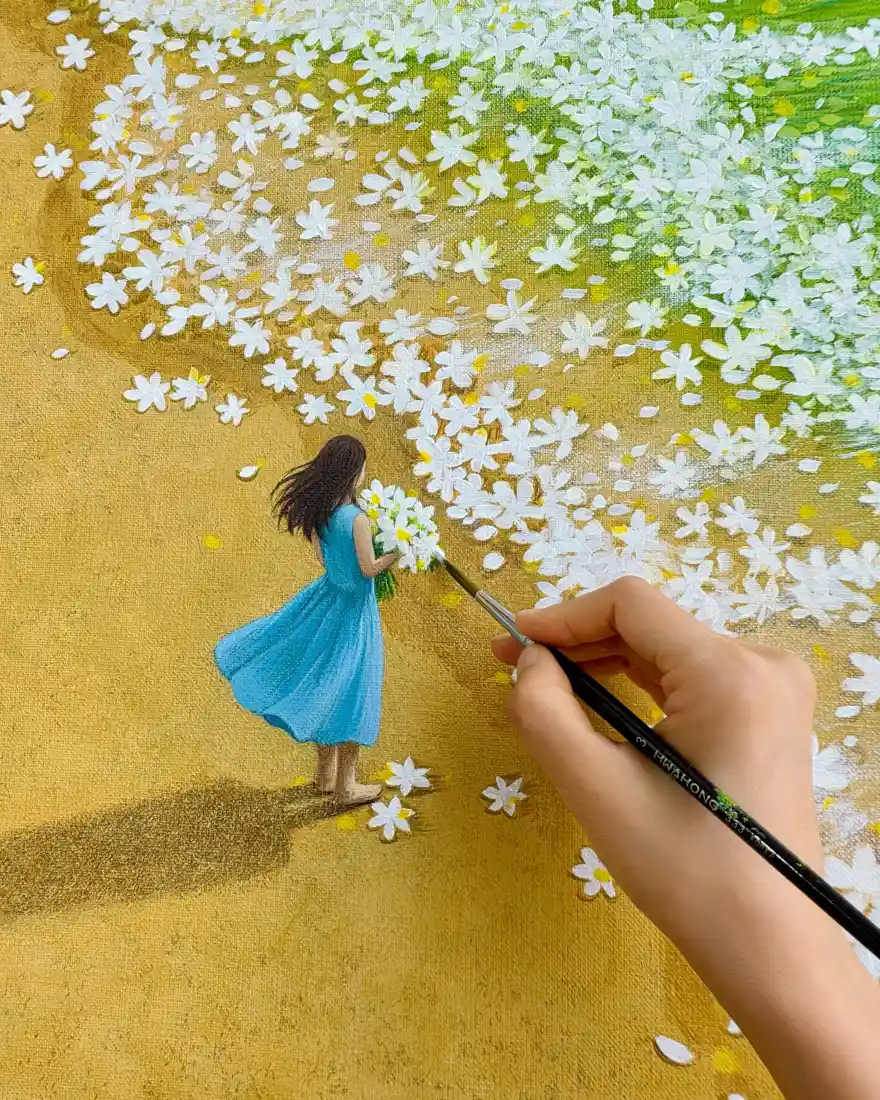 手持画笔在画布上绘制蓝裙少女立于白色小花丛中的治愈场景