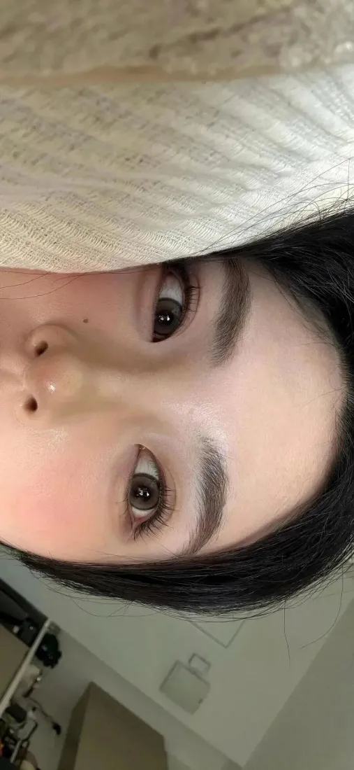 黑发女生倒置脸部特写，卧于浅色织物上，室内自拍视角