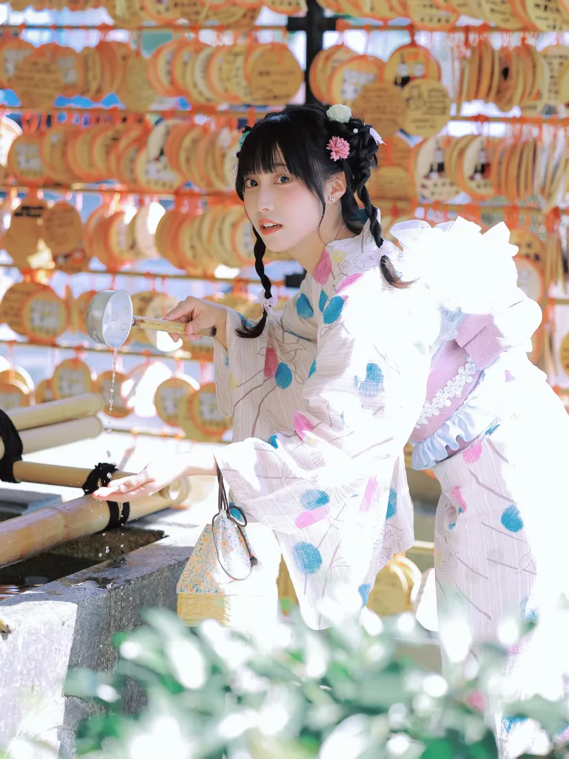 穿粉蓝波点和服的双麻花辫少女在神社手水舍舀水，背景是成片绘马许愿牌。