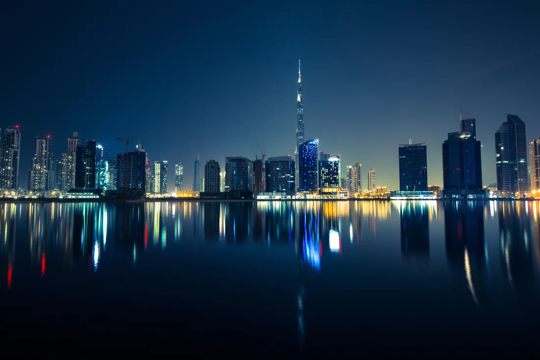 迪拜哈利法塔领衔的城市天际线夜景，水面清晰倒映楼宇灯火