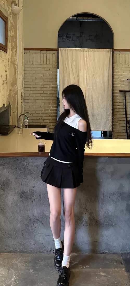 黑长直少女穿露肩上衣与百褶短裙，站在咖啡馆吧台旁手持饮品。