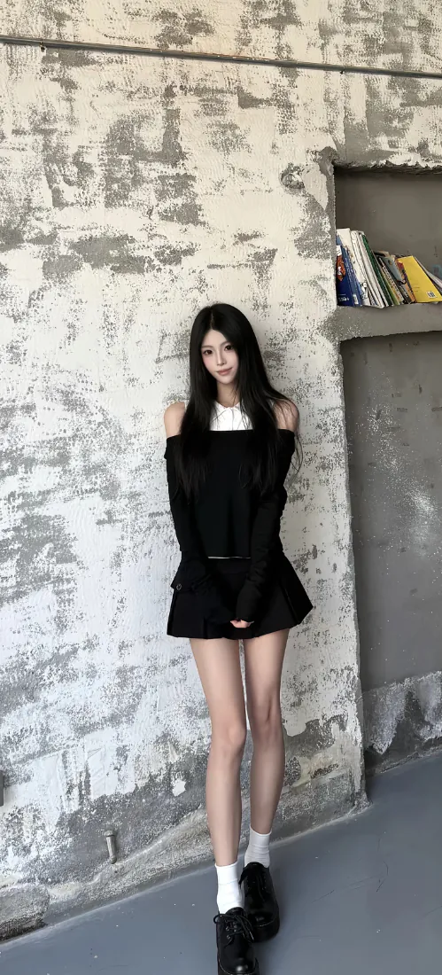 黑长直少女穿露肩黑裙白袜黑鞋，站在斑驳水泥墙前。