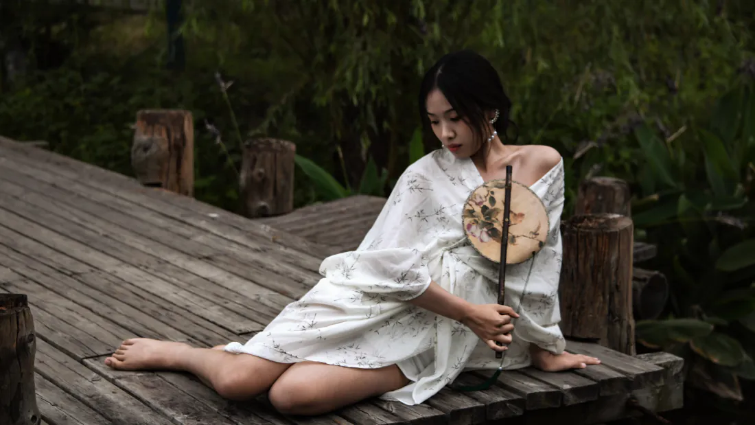 8k古风美女壁纸|白衣女子坐木栈道背景图片 - 清幽国风「哲风壁纸」 白衣女子赤脚坐木栈道,手持团扇,身后是茂密绿植