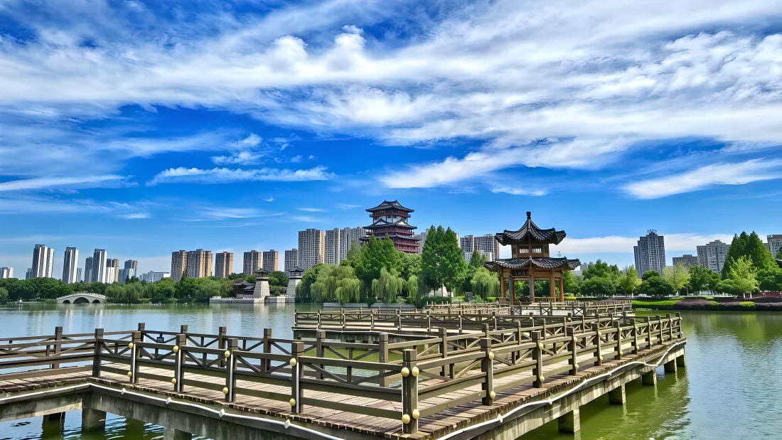 4k湖景壁纸|湖畔木栈道古亭背景图片 - 清新城市风光「哲风壁纸」 晴朗白日下的城市湖泊,前景木栈道延伸向水面,远处古亭楼阁与城市高楼相映。
