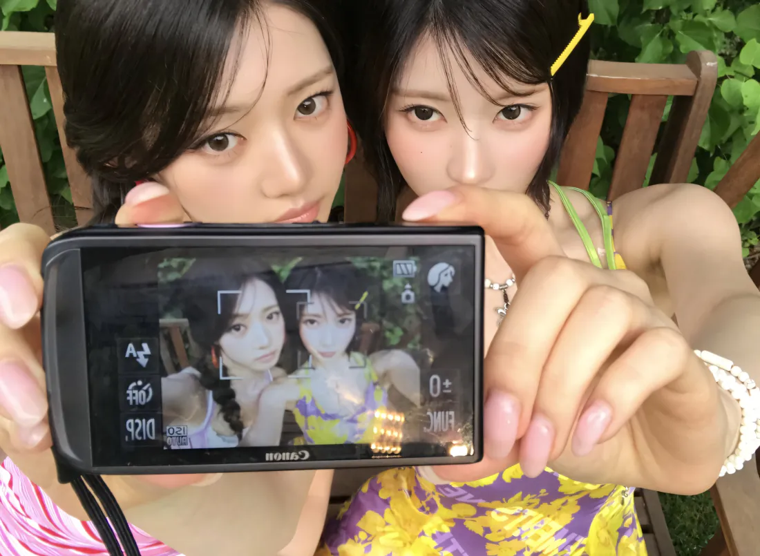 2kBABYMONSTER壁纸|双人自拍相机背景图片 - 清新日常「哲风壁纸」 两位年轻女生手持数码相机自拍,身后是户外绿植与木椅,氛围清新日常。