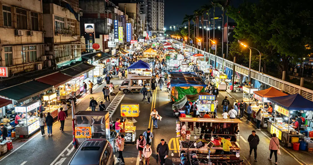 夜晚城市街道两侧摆满小吃摊位，人流穿梭，灯火通明充满市井烟火气