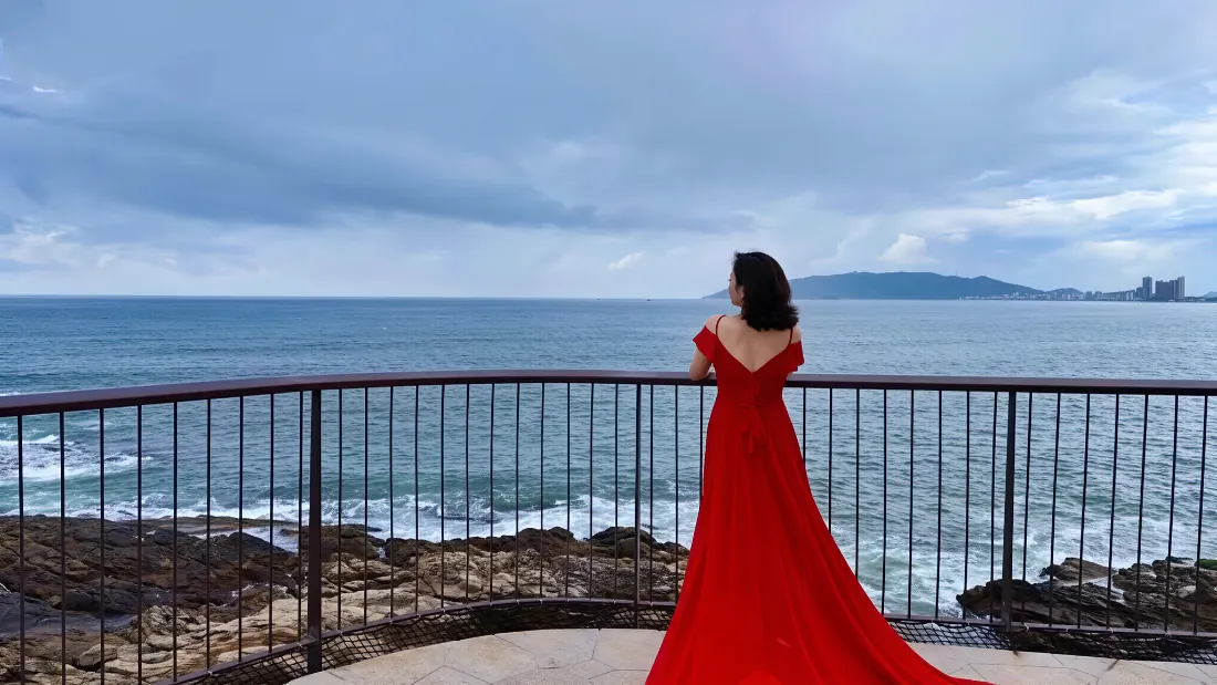 2k红衣美女壁纸|海边观景台远眺海景背景图片 - 清新治愈「哲风壁纸」 穿红色露背拖尾长裙的短发女子背对镜头,倚靠海边观景台护栏眺望海面。