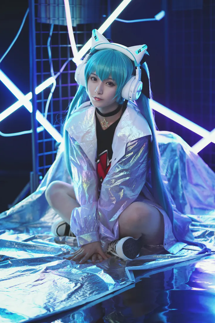 蓝发双马尾初音未来coser蹲坐于霓虹蓝调赛博风室内场景，佩戴猫耳耳机。