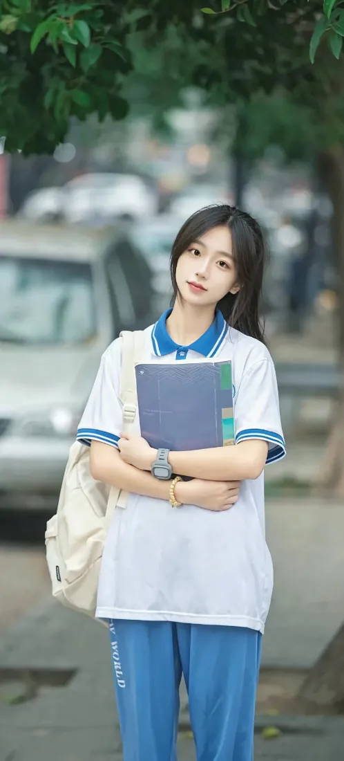 户外街道旁，穿蓝白校服的黑发少女抱文件夹站立，背景虚化有树木车辆。