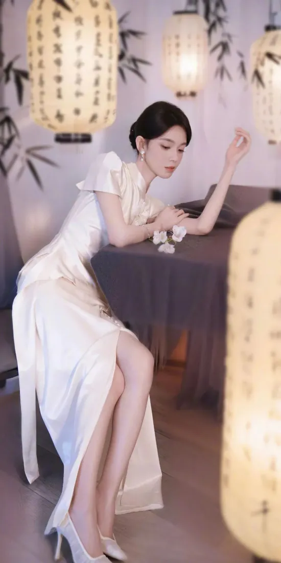 身着白色开叉旗袍的女子倚靠桌沿，周围悬挂带书法的中式灯笼，背景绘有墨竹。
