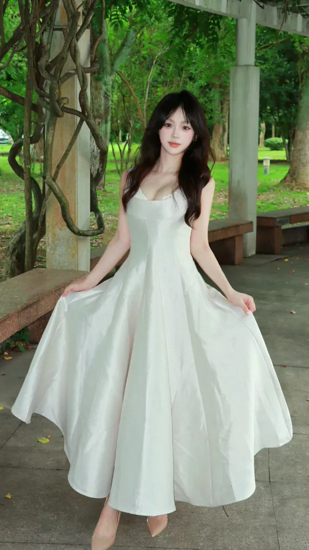 穿白色吊带长裙的长发女生站在公园凉亭下，双手轻提裙摆，背景是葱郁绿树草地。