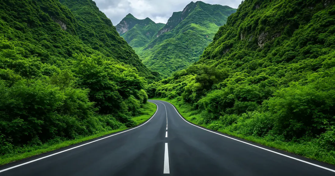 蜿蜒柏油公路穿行于两侧翠绿山林山谷间，远处层叠青山与多云天空相映。