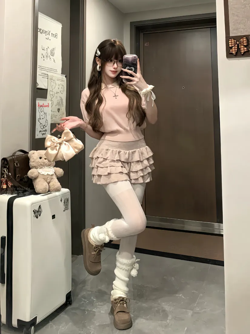 甜系少女在居家走廊镜前自拍，身着粉色套装搭配白丝堆堆袜，旁侧行李箱摆放毛绒小熊。