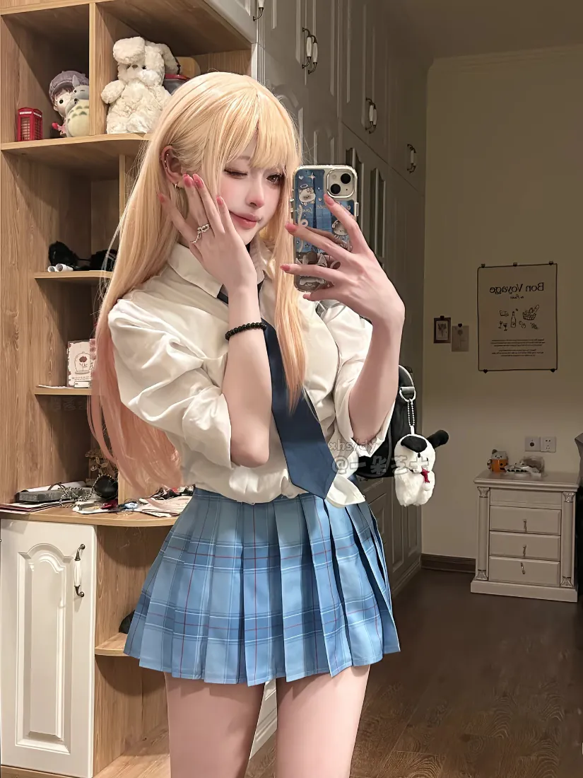 金发双马尾少女穿JK制服在居家房间对镜自拍，身后是木质置物架与白色家具