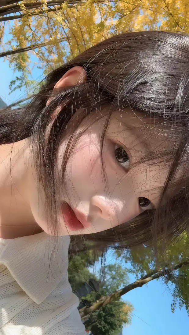 秋日户外，齐刘海少女在银杏树下自拍，背景是蓝天与黄叶。