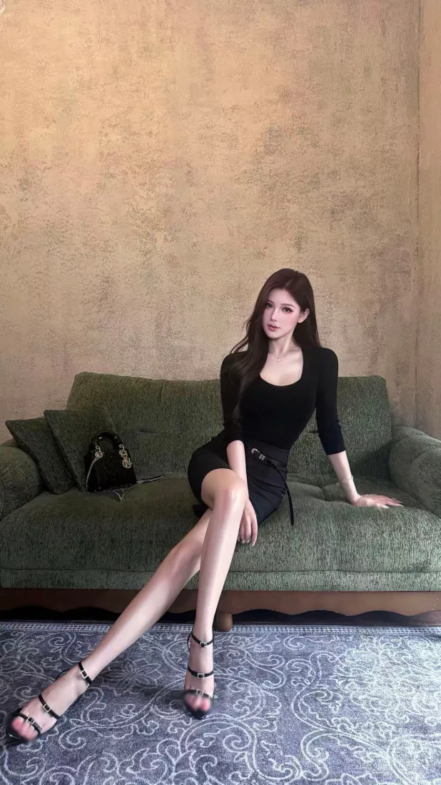 黑衣长发女子坐于绿色沙发上，双腿舒展，脚穿黑色细带高跟凉鞋。