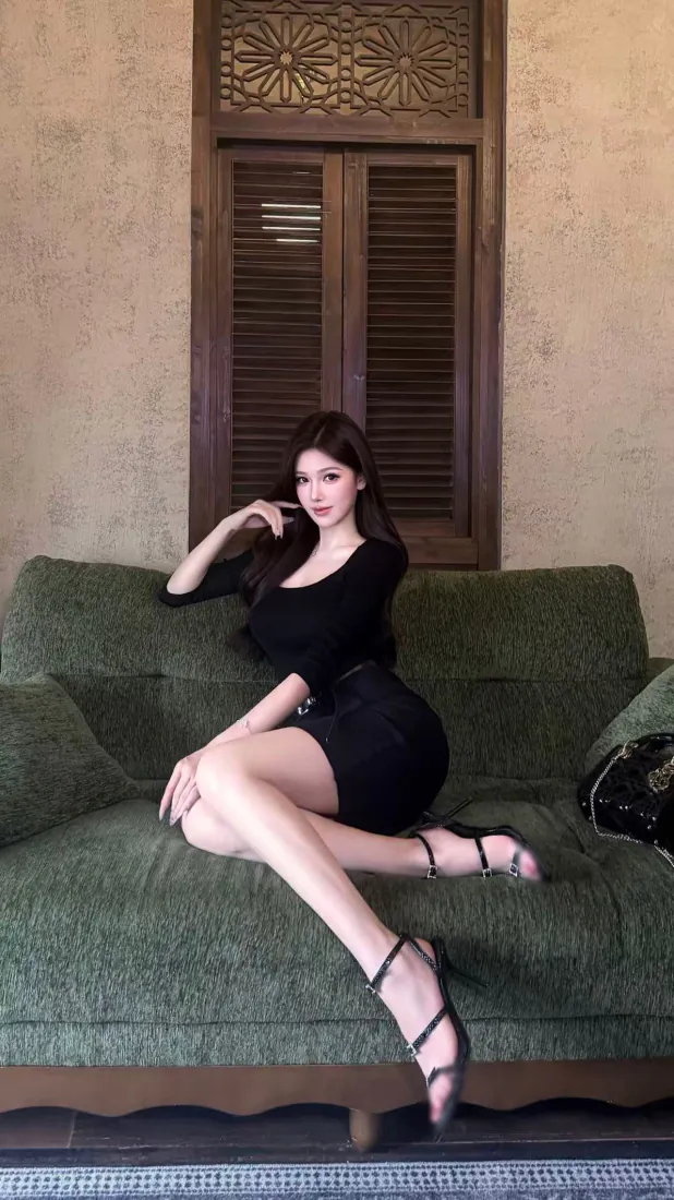 身着黑色包臀裙的长发女子斜倚在复古绿色沙发上，身后是雕花木质百叶门。