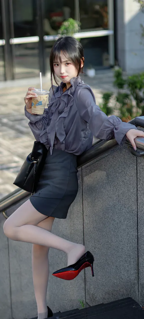 年轻女子倚石护栏，手持冰咖啡，穿灰紫衬衫与包臀短裙，红底高跟鞋。